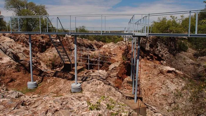 red, exposed soils under a network of metal walkways, with green vegetation around