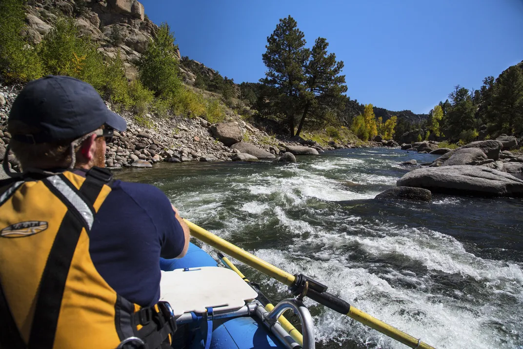 Back of a man in a whitewater rafting vessel on a river