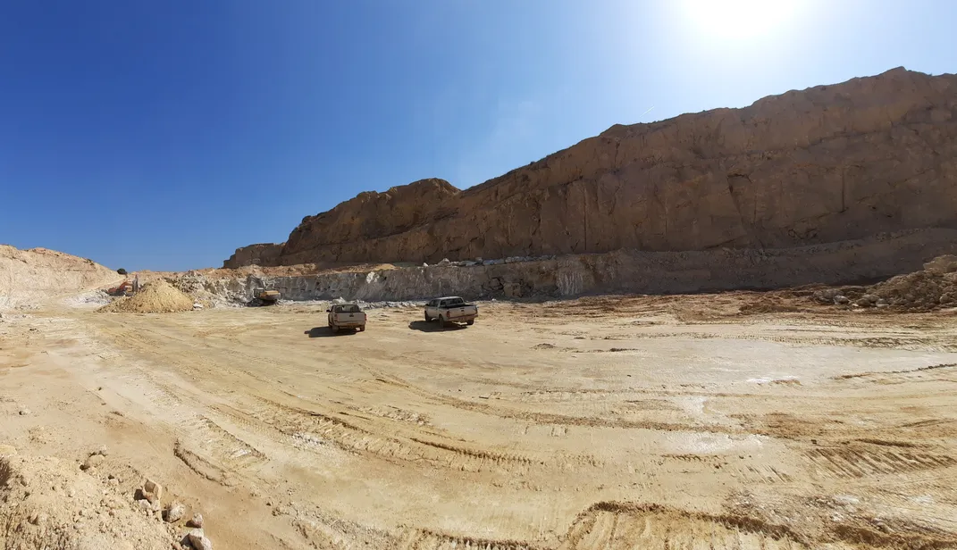landscape image of dry land in a quarry with a cut mountainside in the background and two pickup trucks