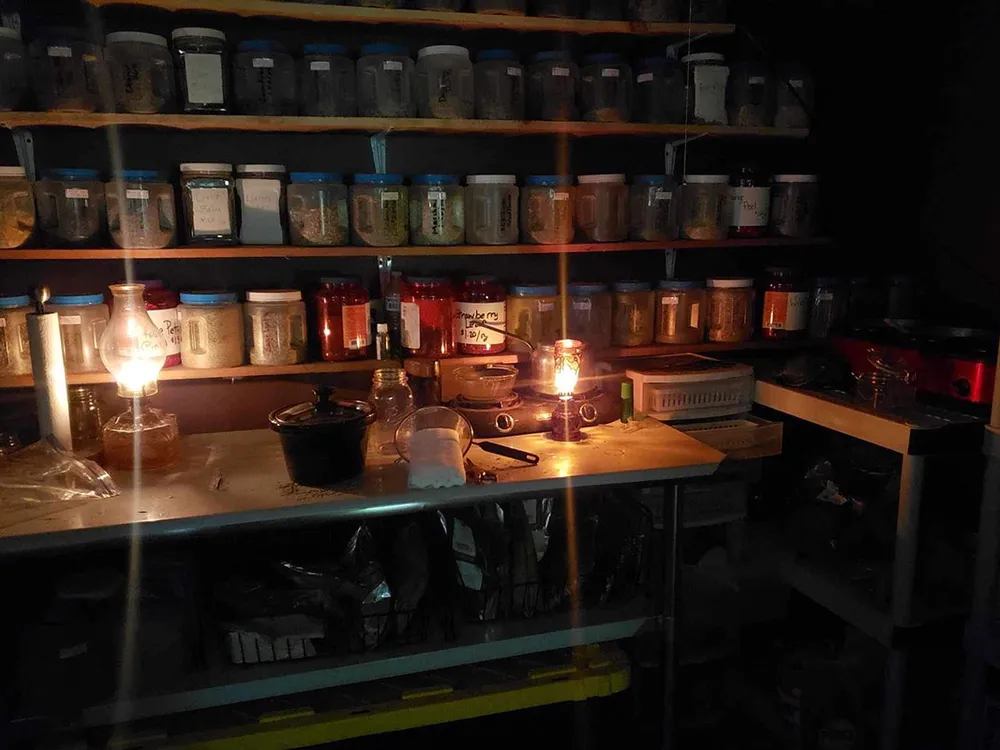 Wooden shelves and counter filled with jars are lit by two oil lamps.