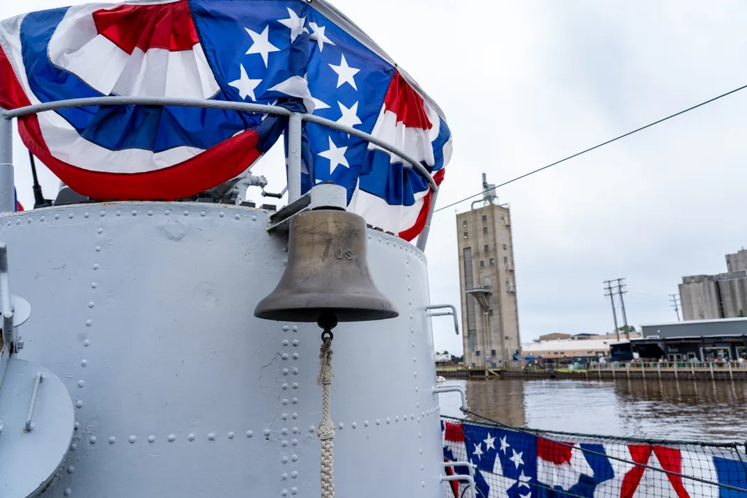 Bell hanging from submarine next to patriotic buntig