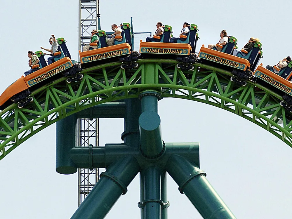 People riding orange carts at the top of a green roller coaster