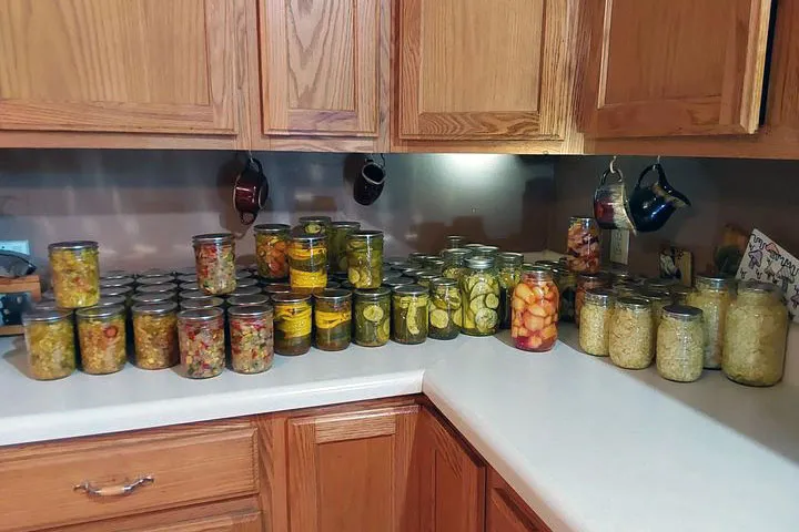 On a kitchen counter, jars of pickles and other concoctions.