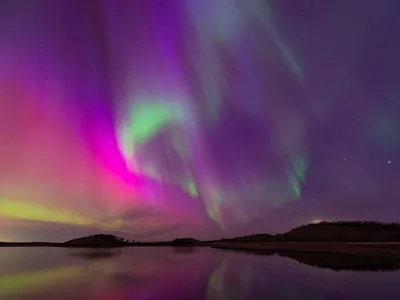 purple and green streaks in the air over water and mountains at night